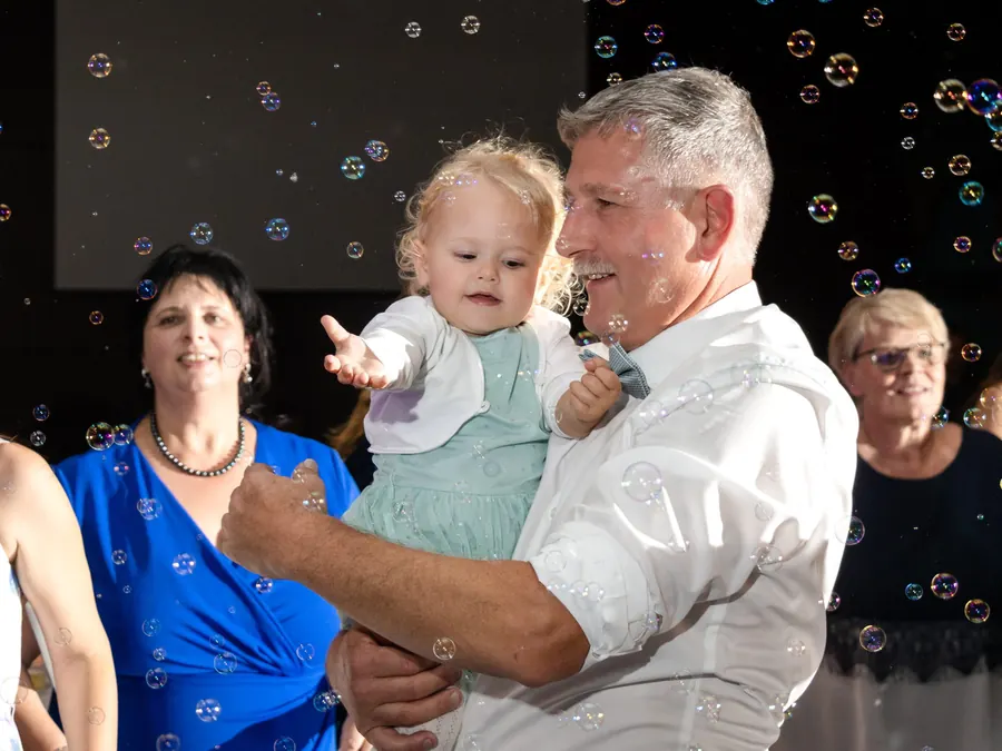 Großvater tanzt mit Enkelkind im Seifenblasenregen, ausgelassene Hochzeitsparty