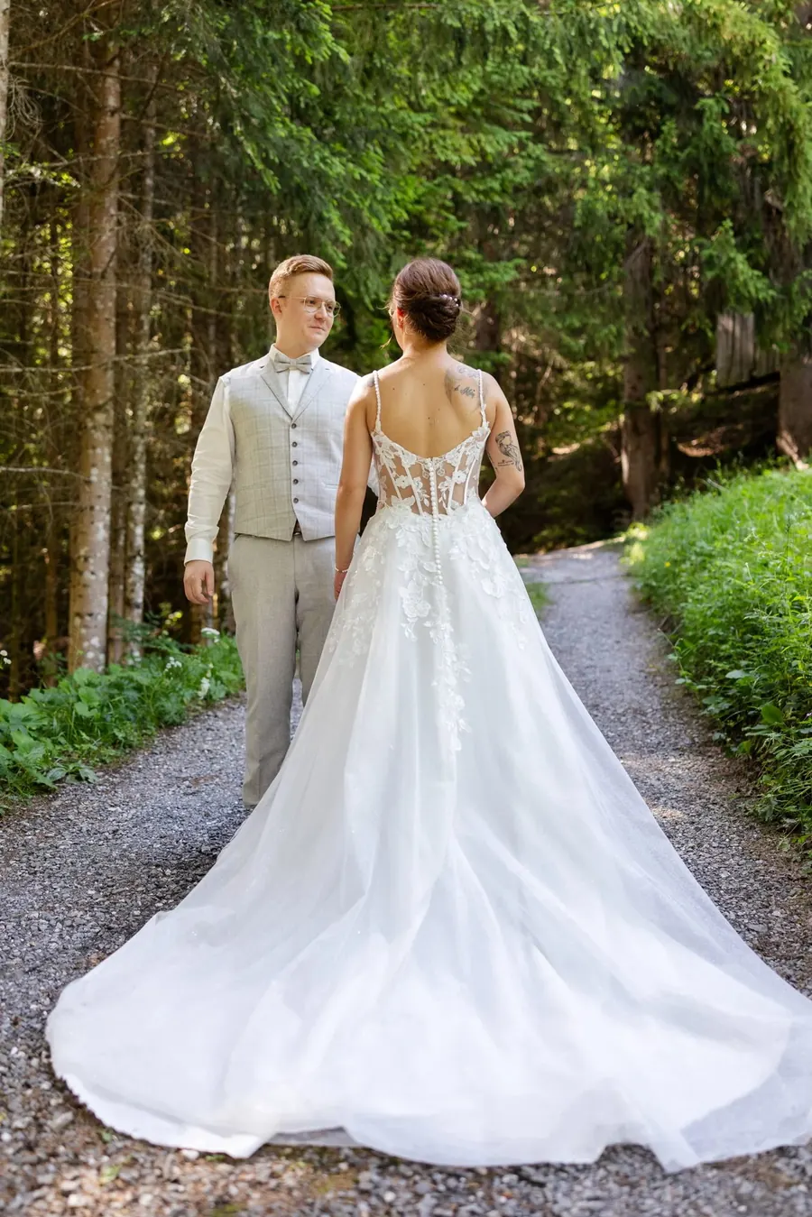 Brautpaar spaziert auf einem Waldweg, Braut im Spitzenkleid mit langer Schleppe