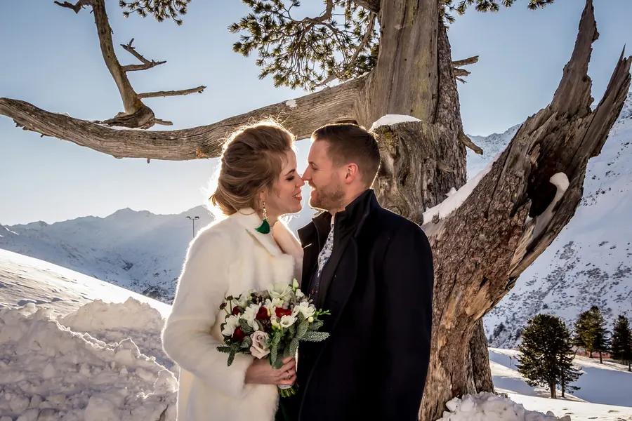 Brautpaar küsst sich vor verschneiten Gipfeln, Winterhochzeit in Lech am Arlberg