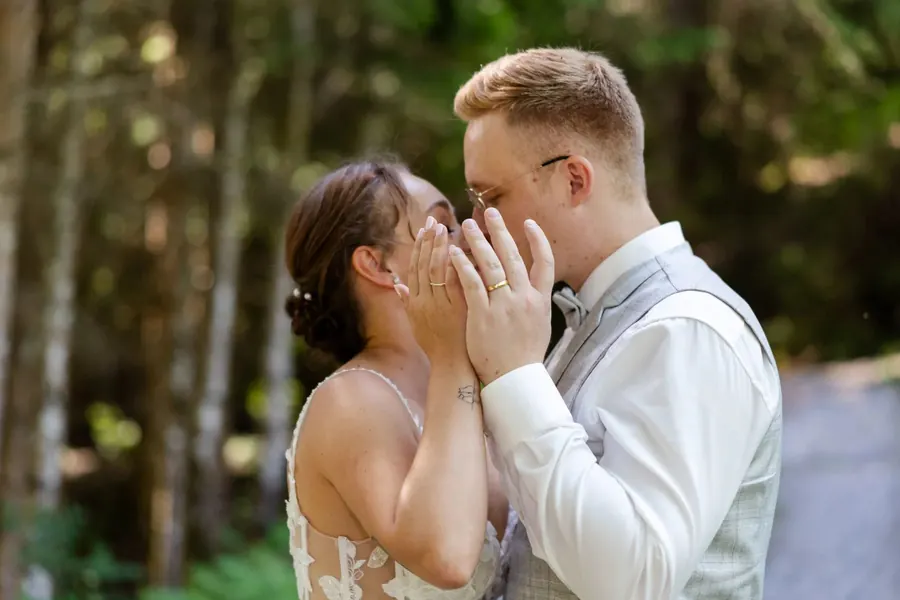 Brautpaar küsst sich hinter den Händen, Trauringe im Detail, Hochzeit im Wald