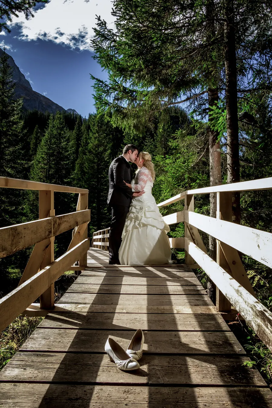 Brautpaar küsst sich auf einer Holzbrücke im Bergwald, Hochzeit in den Alpen