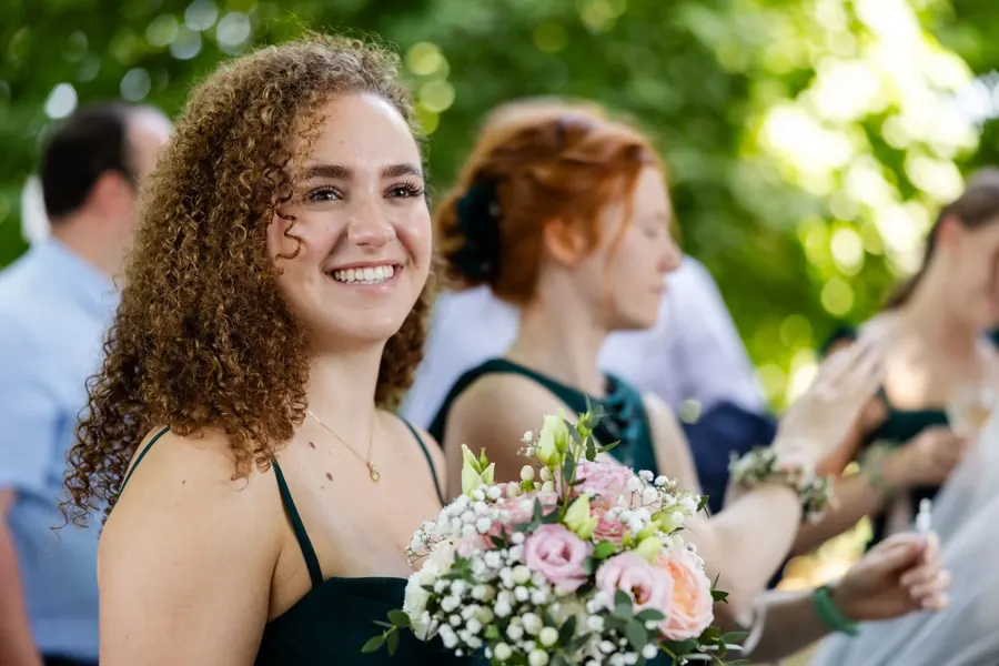 Brautjungfer mit Brautstrauß lächelt beim Sektempfang, Sommerhochzeit im Grünen