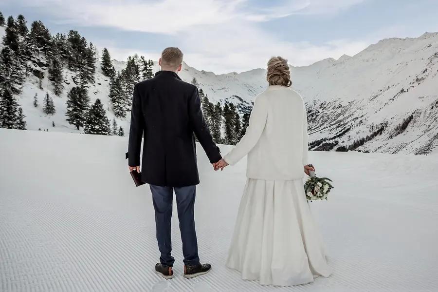 Brautpaar Hand in Hand im Schnee mit Blick auf die Alpen, Winterhochzeit in Tirol